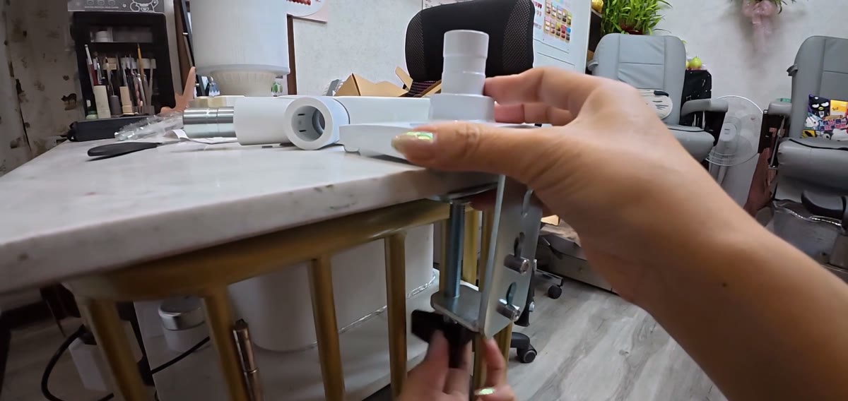 Xiao Cui's hands tightening a metal clamp under the edge of her marble nail desk