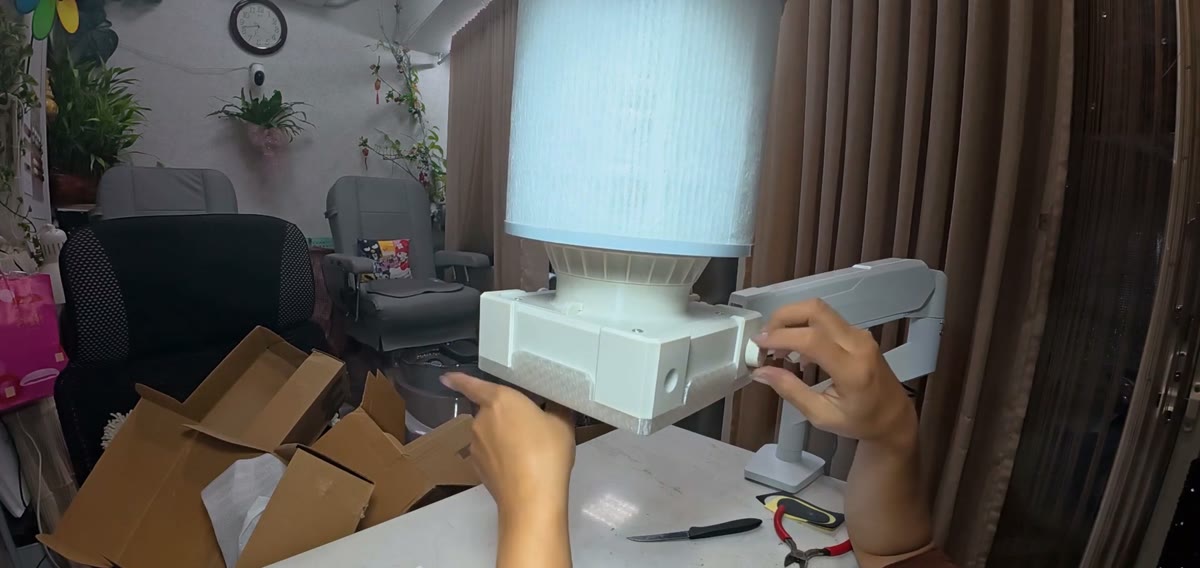 A white nail dust collector with a tall filter and adjustable arm clamped to a nail desk